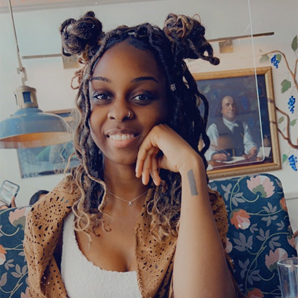 Smiling woman with braided hair seated in a restaurant with a painting in the background.