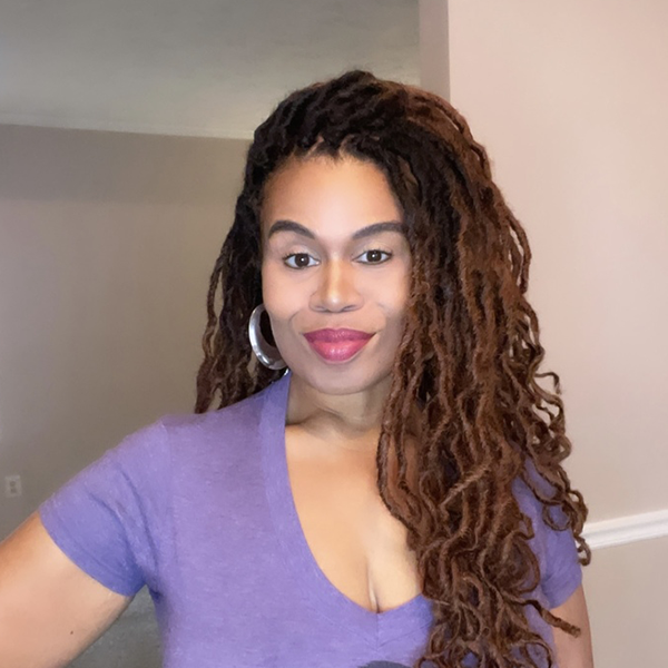 Woman with long curly hair and a purple shirt smiling indoors.