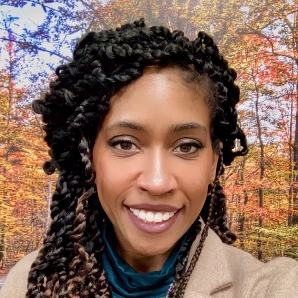 Smiling person with braided hair in front of a colorful autumn forest background.